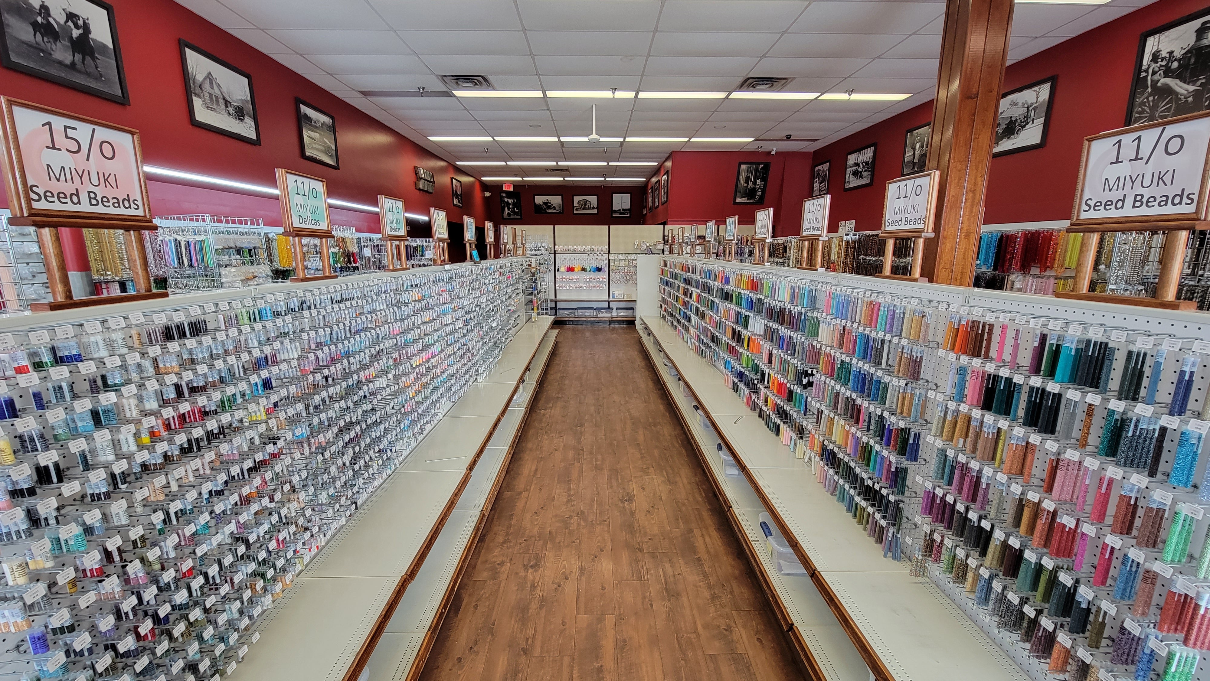 Inside view of the Bead Abode retail hobby store taken from front lobby showing main aisle of seed beads with rocailles along the right side organized by size and multi-shaped beads on the left.